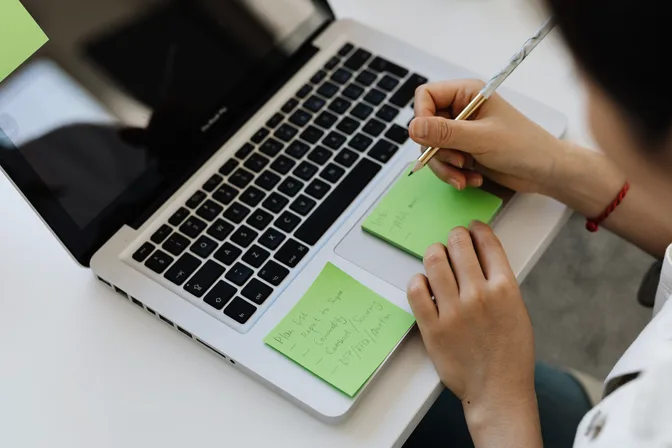 A hand writing on sticky notes beside an open laptop