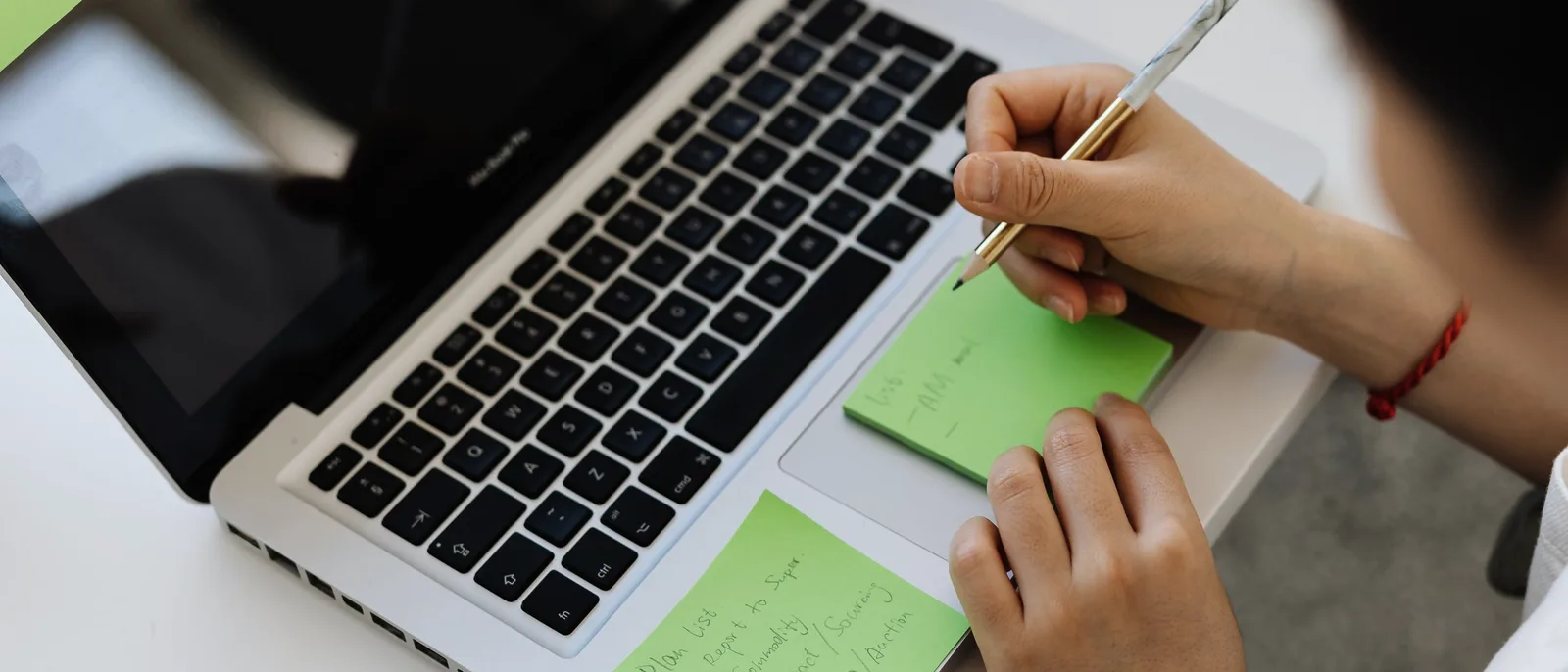 A hand writing on sticky notes beside an open laptop