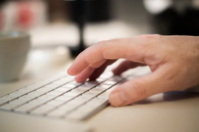 A hand resting on a light keyboard at a desk, in soft daylight