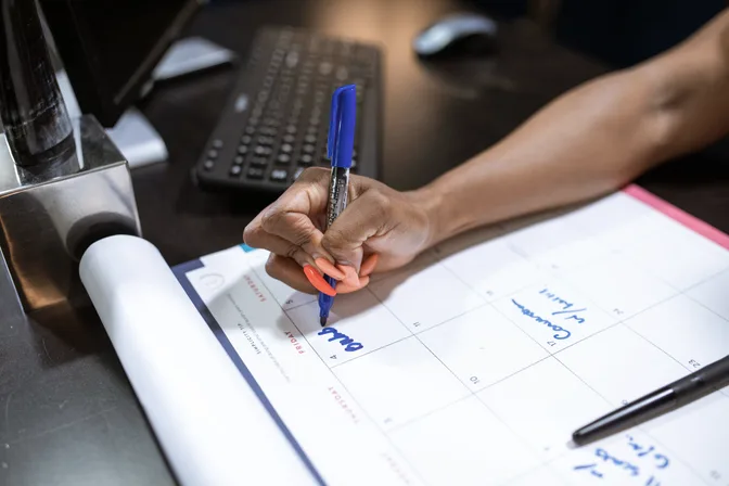 A hand writing dates on a large paper desk calendar