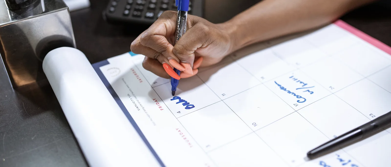 A hand writing dates on a large paper desk calendar