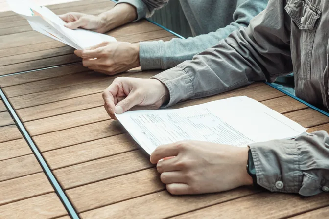 Two people's hands going over printed documents on a wooden table