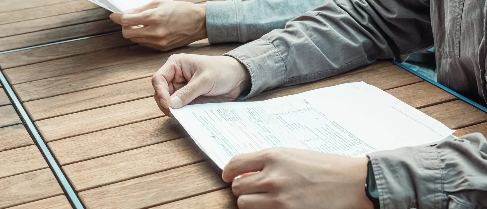 Two people's hands going over printed documents on a wooden table
