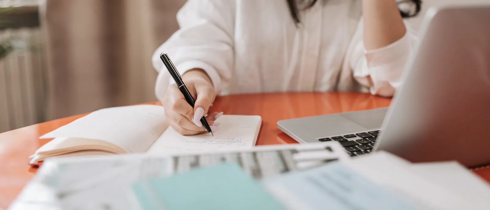 Someone on a phone call, writing notes in a notebook at a desk