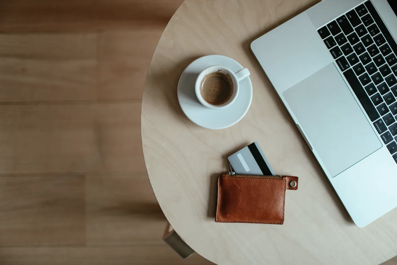 A wallet with a payment card beside a laptop and a cup of coffee, seen from above