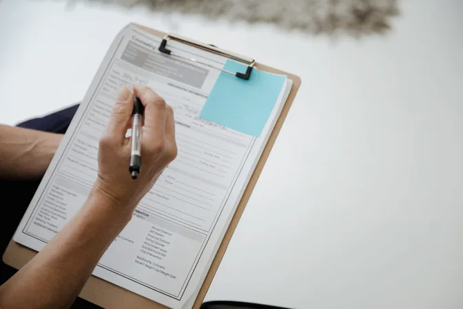 A hand filling in a form on a clipboard