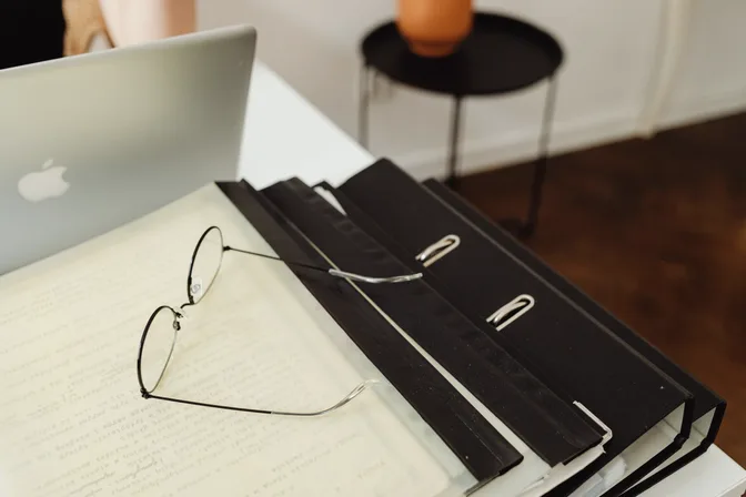 Black ring binders and a pair of glasses resting on papers