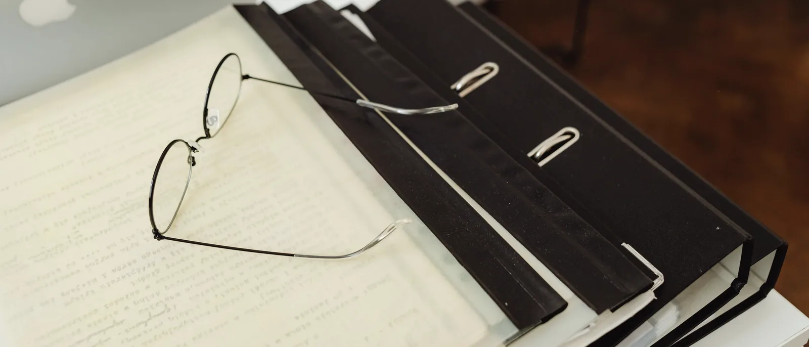 Black ring binders and a pair of glasses resting on papers