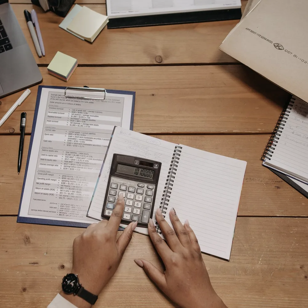 A desk seen from above: printed papers, a calculator, sticky notes and a pair of hands at work